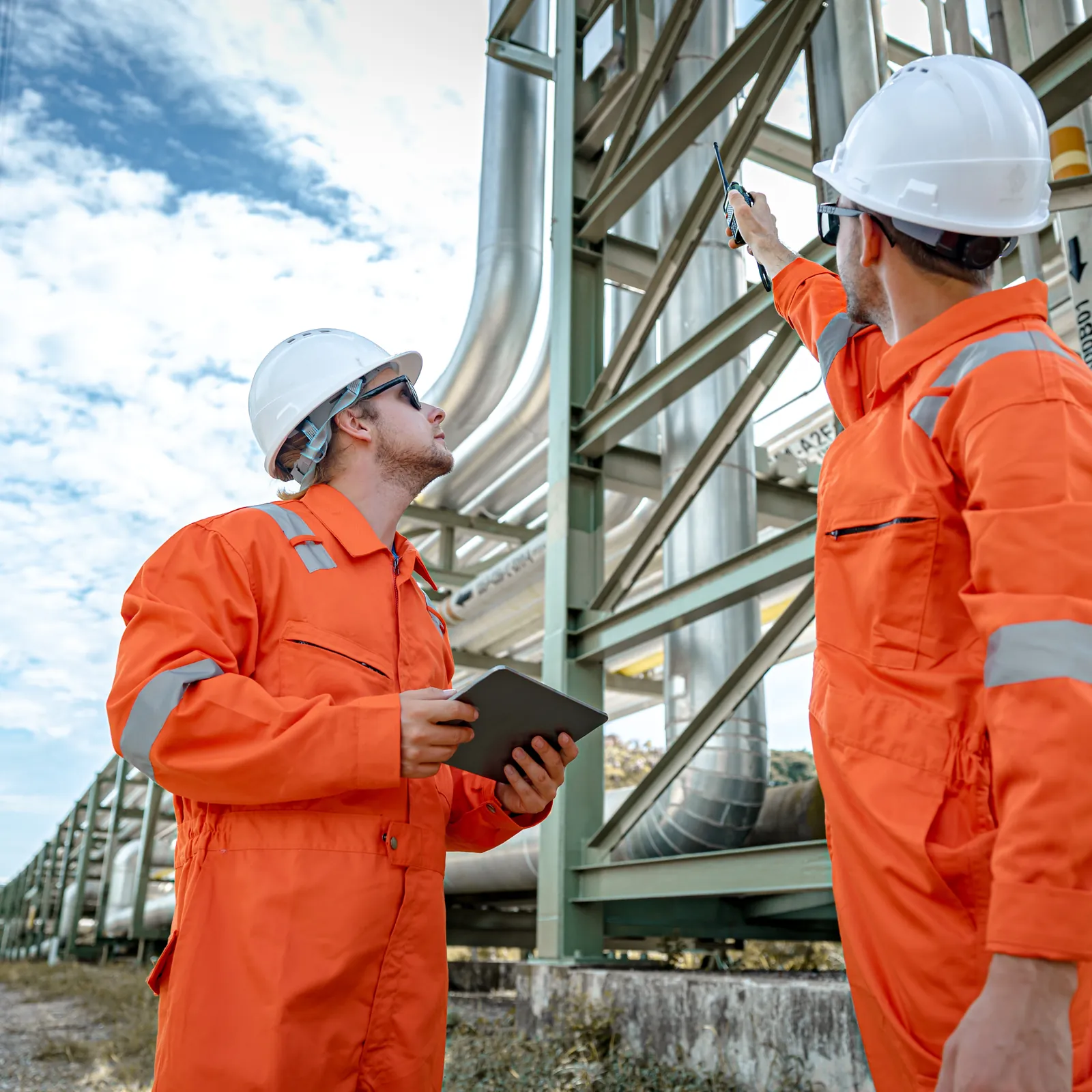 Field technicians in hard hats inspecting an industrial pipe rack (representative image)